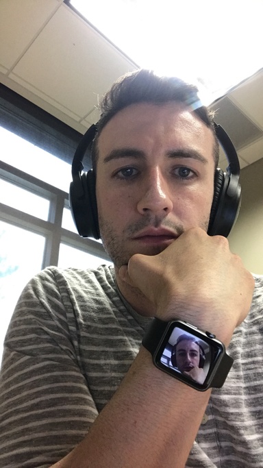 Close up of a man wearing headphones with his own image displayed on his watch. 