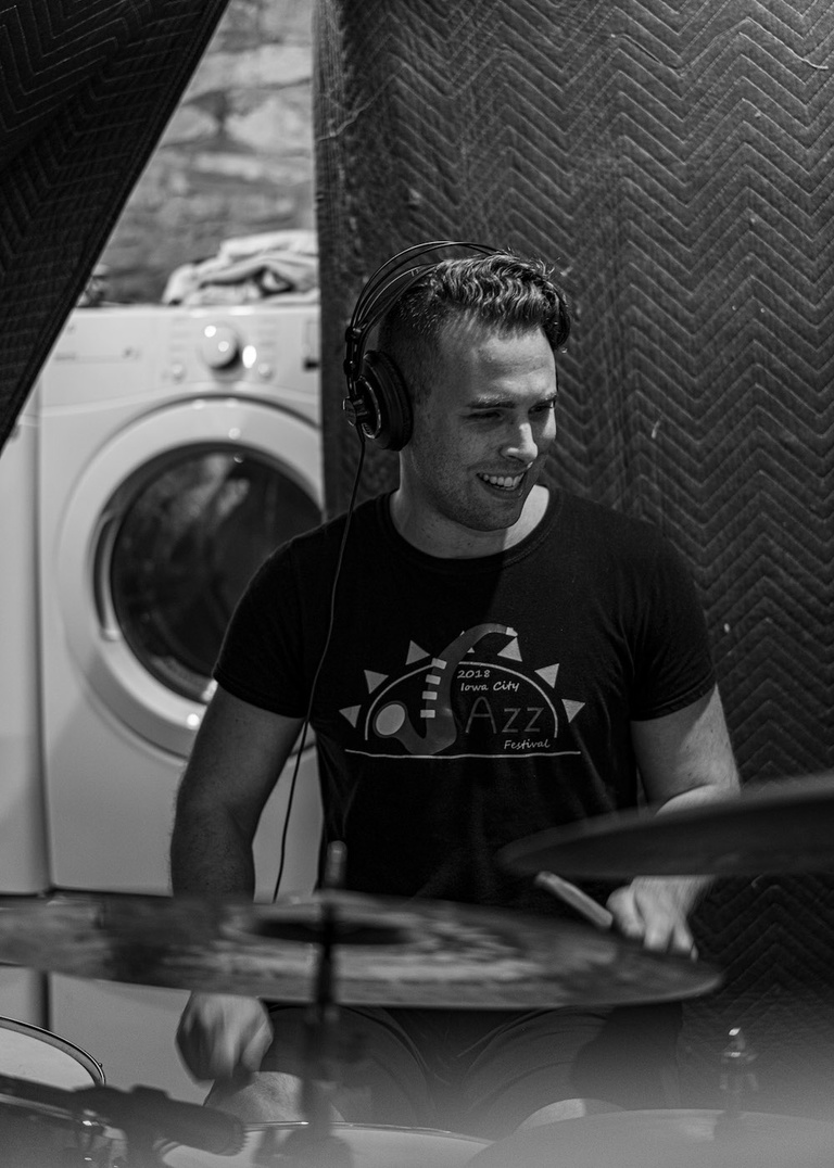 A drummer playing on a drumset with a washing machine in the background. 