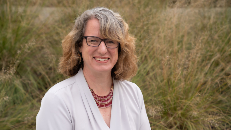 headshot of smiling caucasian woman with glasses and long hair standing in a field. 