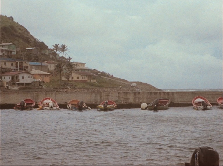 film still: boats on water next to hill with houses