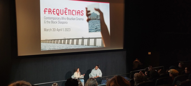 2 black women to a crowd in front of the Frequencias poster on a screen