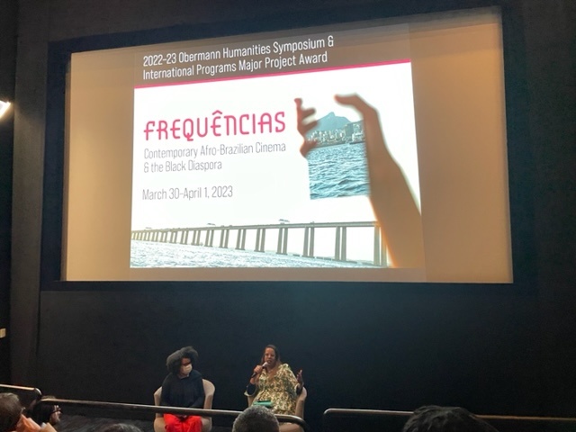 2 black women speaking in front of Frequencias Poster Screen