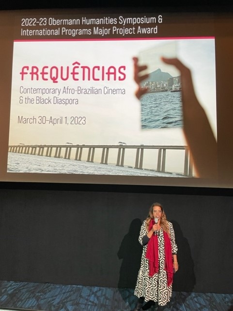 A black woman talking in front of the Frequencias poster