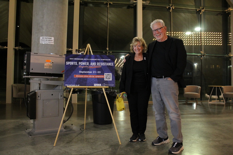 people standing in theatre lobby next to symposium sign