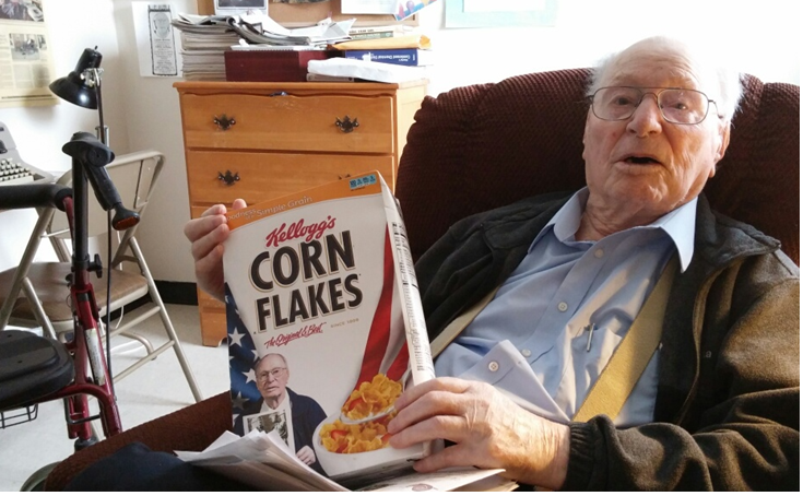 Nursing home resident and WWII veteran holds cereal box with his photo on it