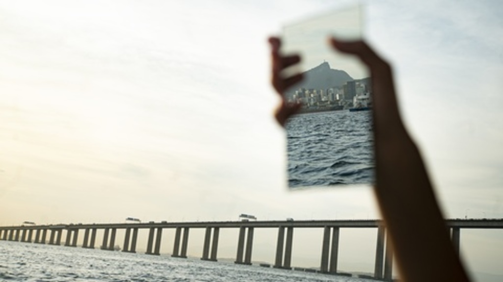 Hand holding up mirror, reflecting peninsula near bridge