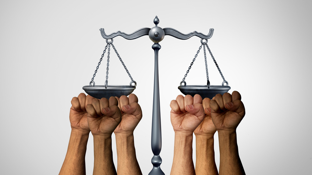 Many multiracial hands holding up both sides of the scales of justice